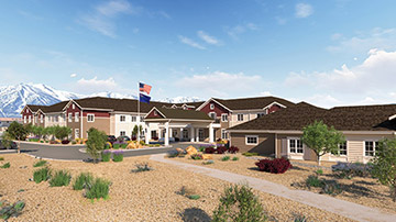 A large, modern Senior Living complex with an American flag, surrounded by landscaped desert plants, set against a backdrop of distant mountains under a blue sky with scattered clouds.